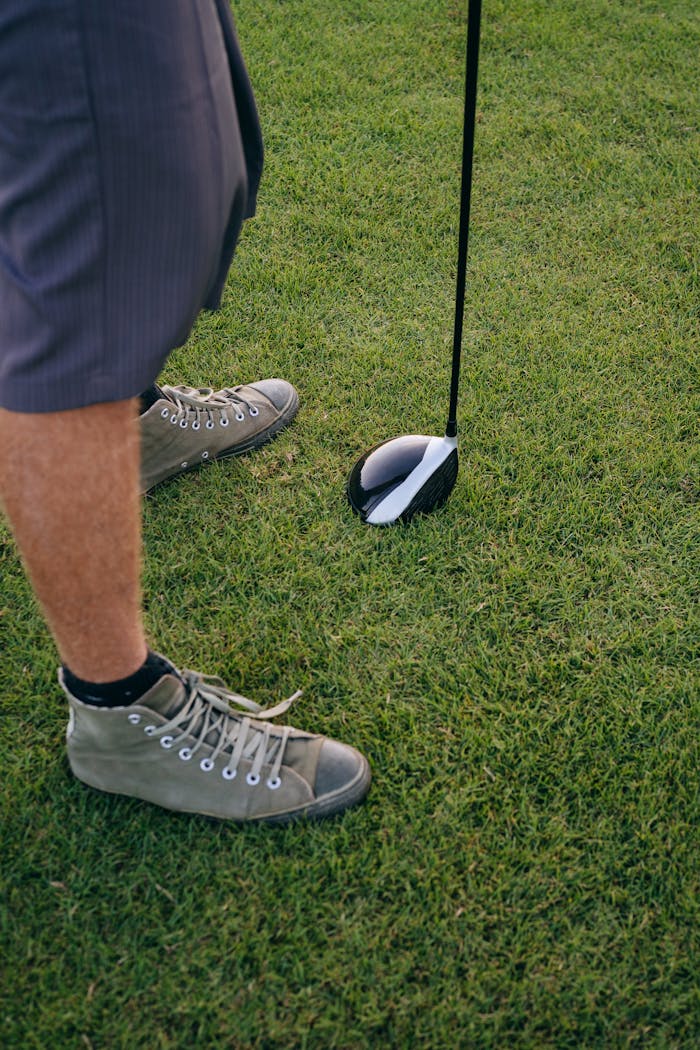 Close-up of a golfer with stylish shoes preparing to tee off on a green course.